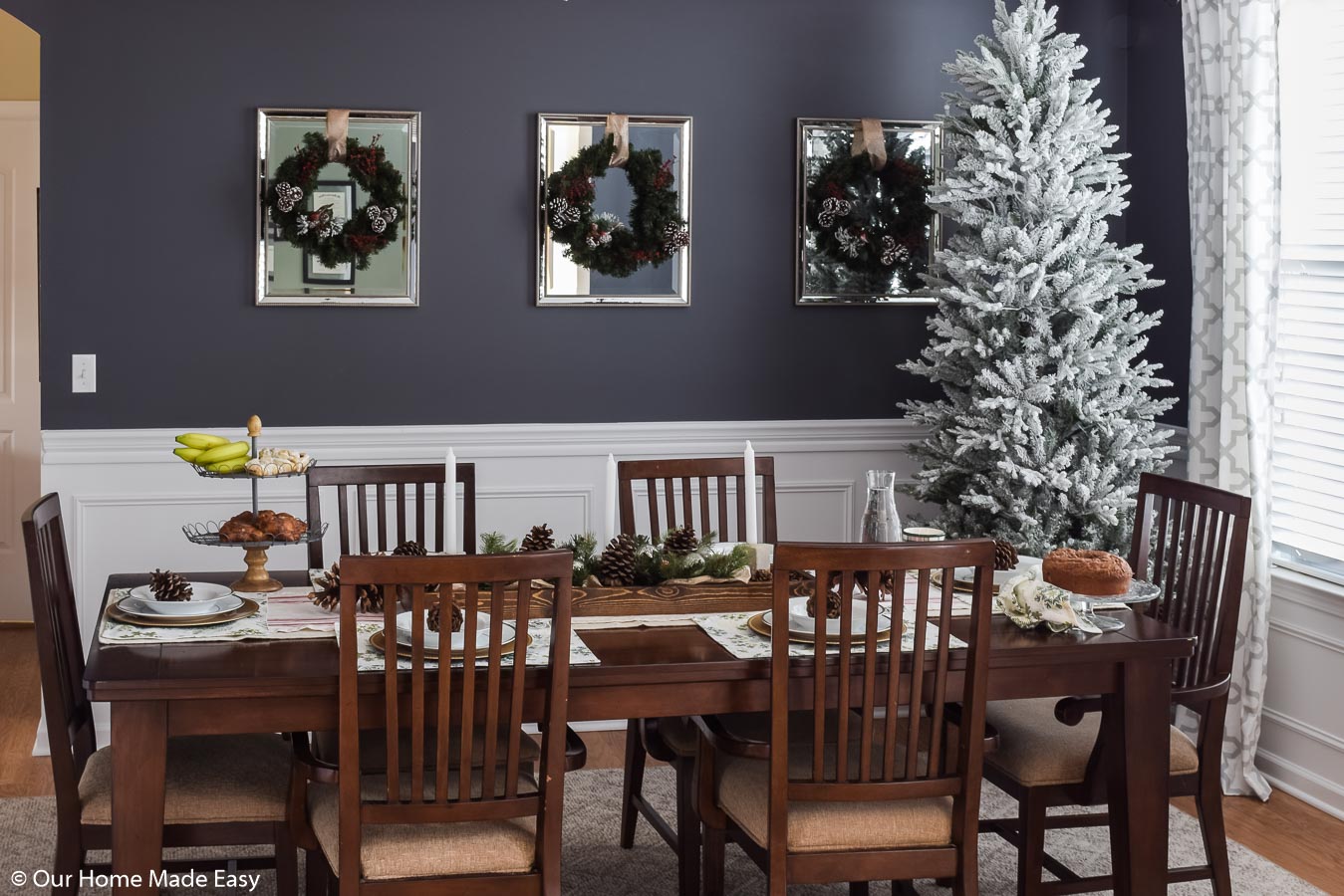 Our festive Christmas dining room is adorned with simple Christmas decor; wreaths, pinecones, and white-frosted Christmas tree