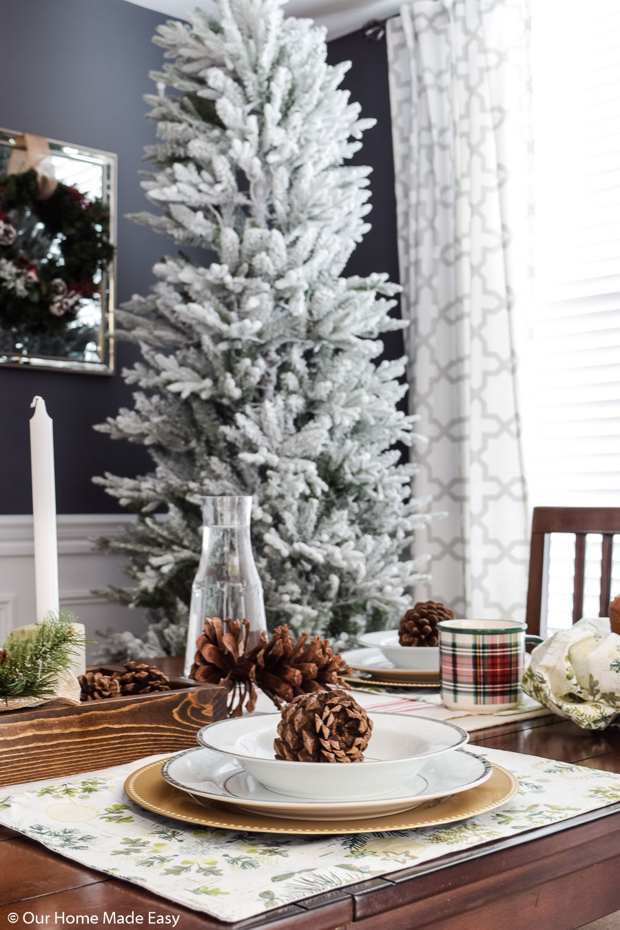 Christmas place settings with gold and white flateware, decorative pinecones, and a white-frosted Christmas tree