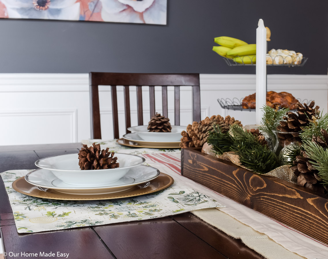 Our festive Christmas dining room place settings are simple white and gold flatware with decorative pine cones