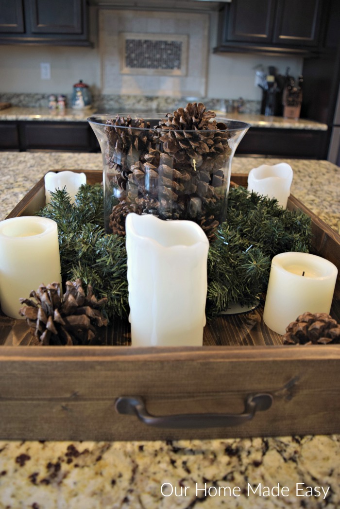 This wood serving tray has festive pinecones, candles, and some Christmas greenery for simple Christmas kitchen decor.