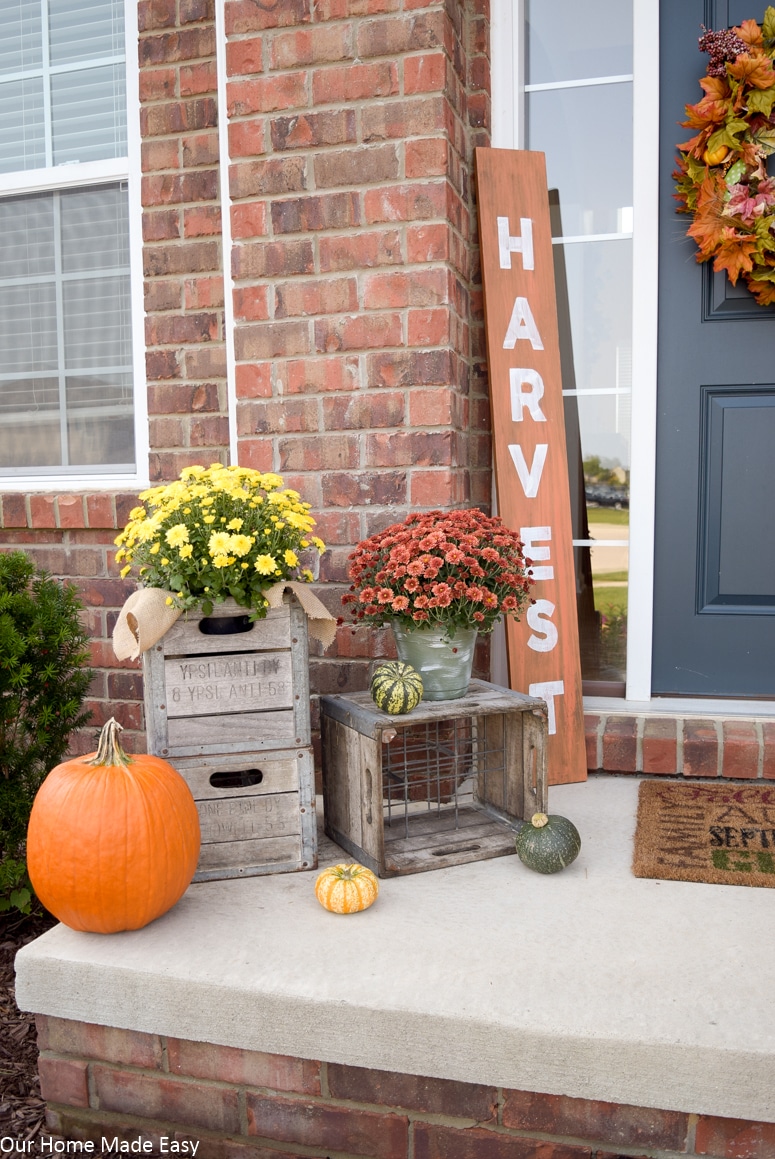 Our rustic fall front porch is complete with pumpkins, bright fall flowers, and a DIY fall harvest sign