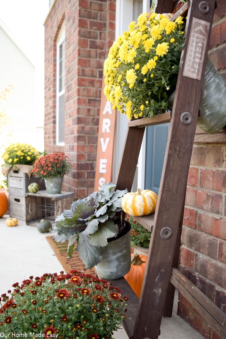 A rustic wood latter decorated with yellow and red mums and mini pumpkins