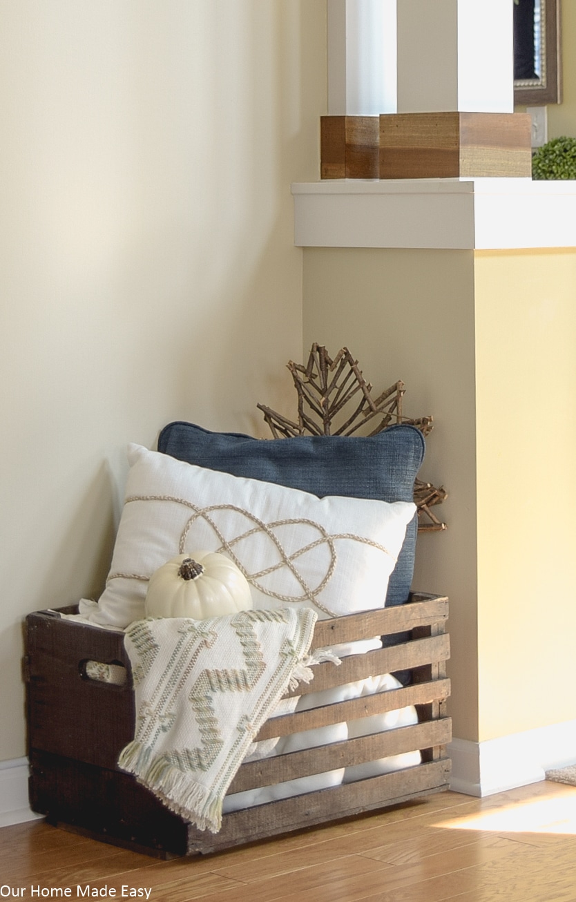 This wooden crate with fall themed throw pillows and pumpkins is an easy way to decorate your home for fall