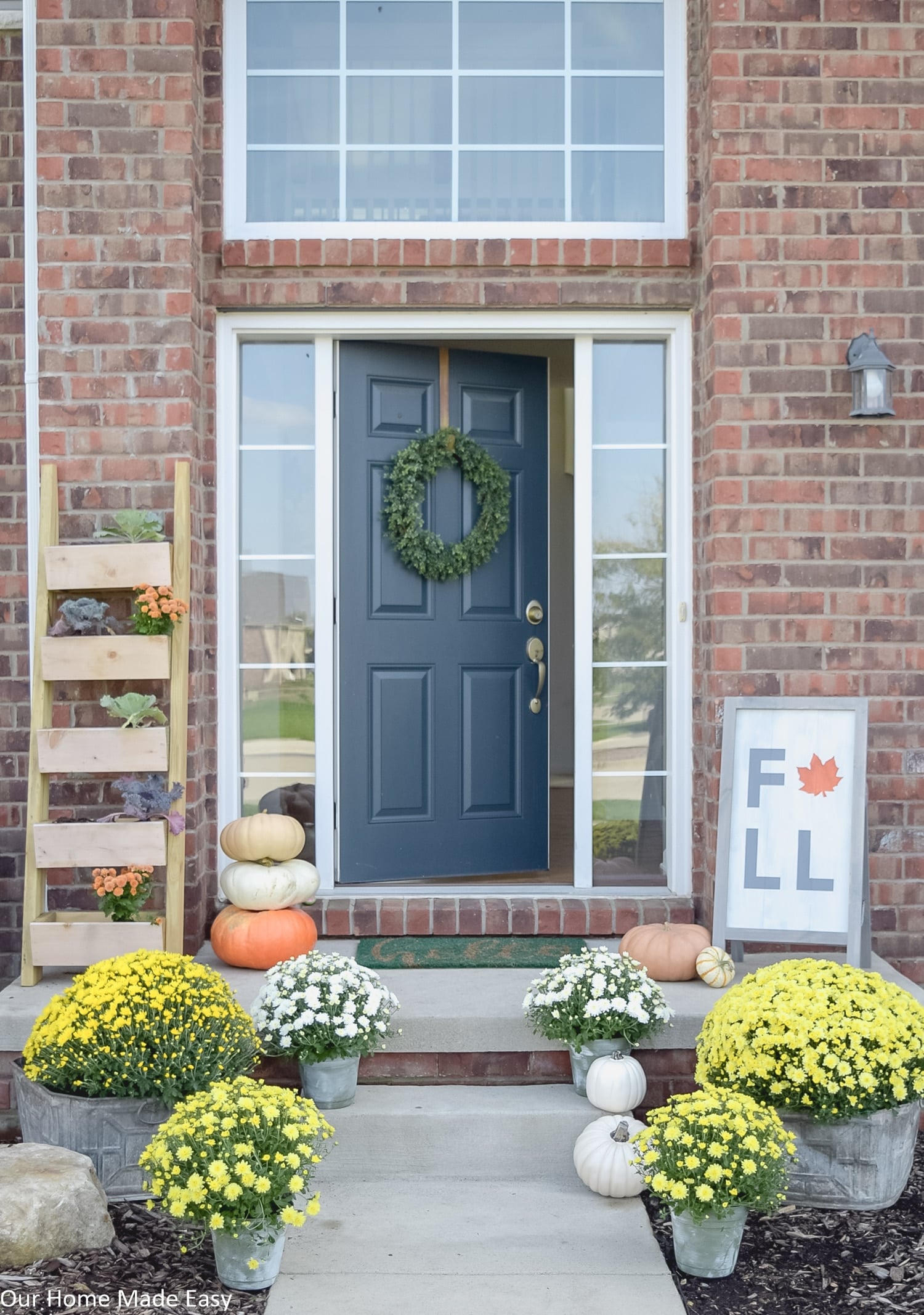 this fall themed front porch is decorated with yellow and white potted mums and harvest pumpkins