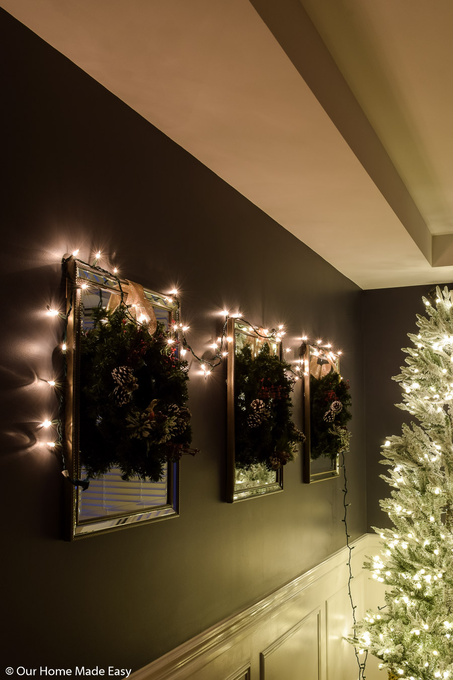 Pine wreaths with simple bows hang over decorative mirrors, with a single strand of bright white Christmas lights 