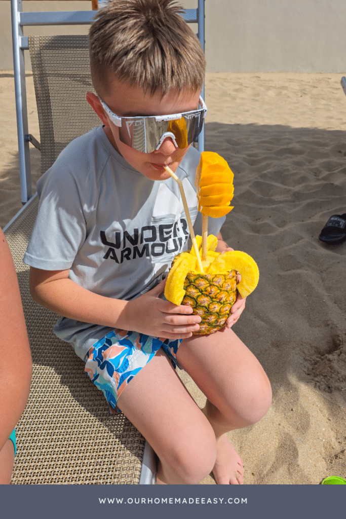 Boy drinking pina colada mocktail out of fresh pineapple on beach